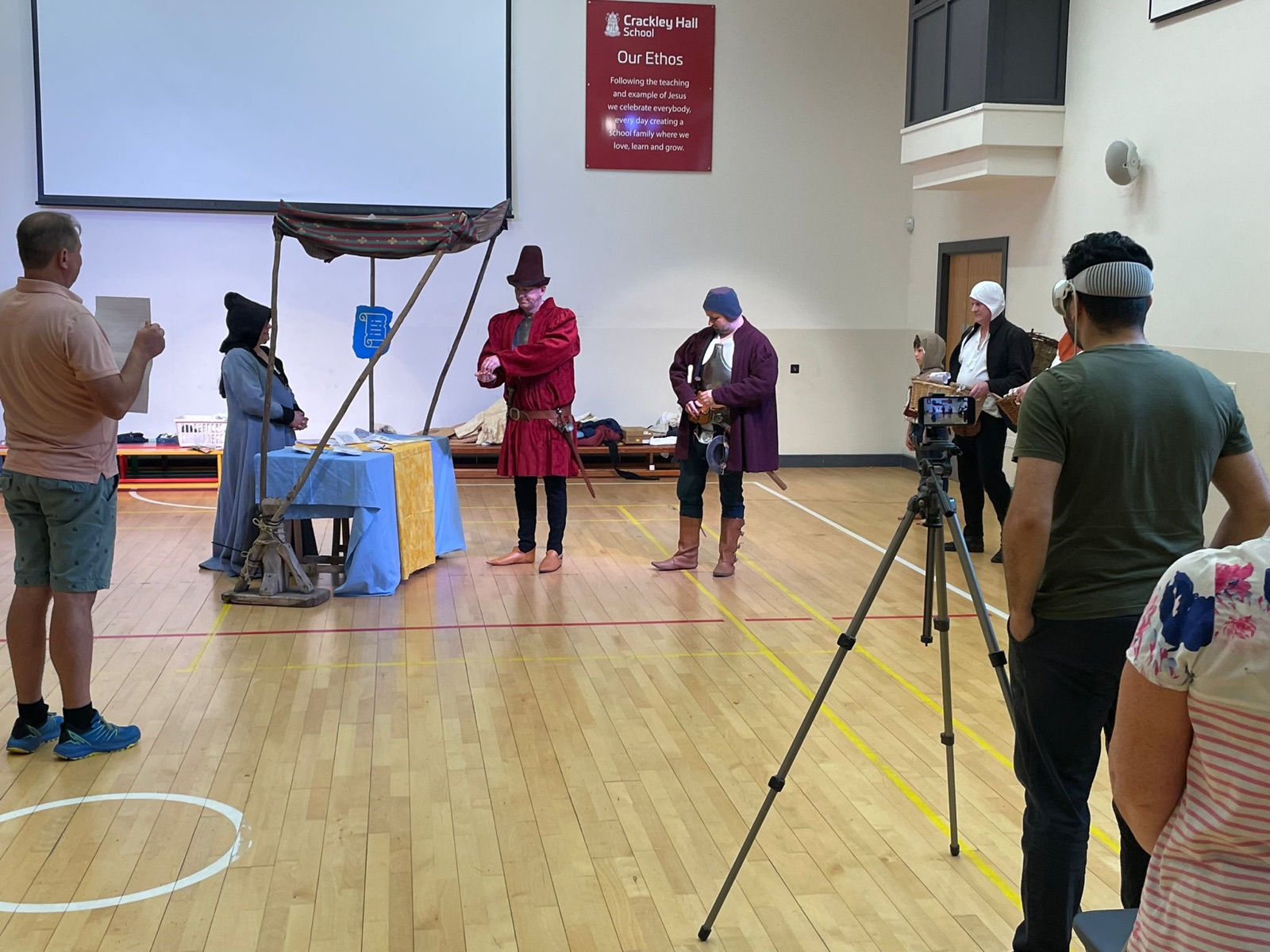 Filming costumed reenactors performing a historical scene in a school hall
